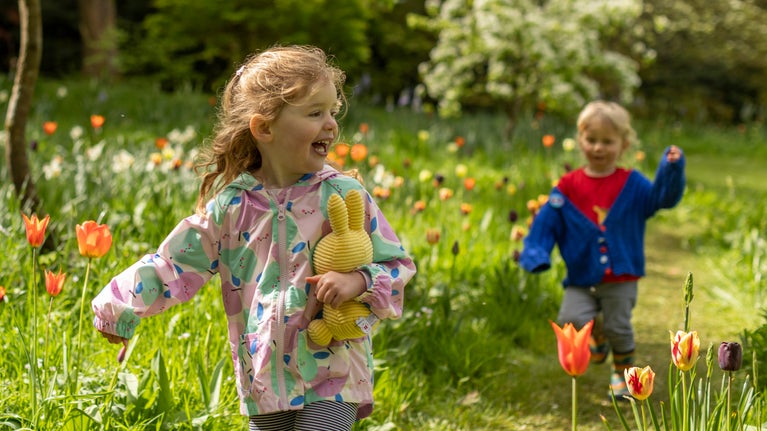 Two children walking along a grassy path surrounded by colourful tulips